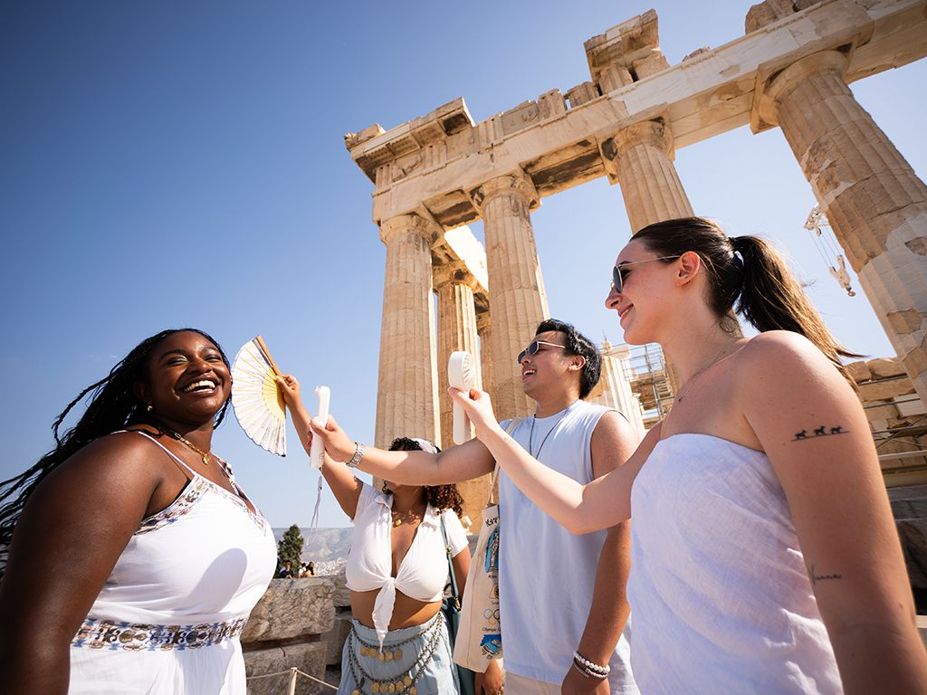 A group of people enjoying a sunny day at the Parthenon, holding hand fans and smiling in front of the ancient columns.