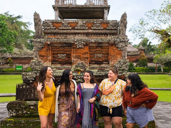 Five people stand smiling in front of an intricately carved stone and brick structure in a lush park setting.