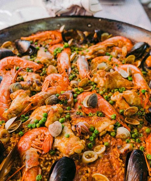 A pan of seafood paella with prawns, mussels, clams, green peas, and rice, garnished with herbs, displayed on a table.