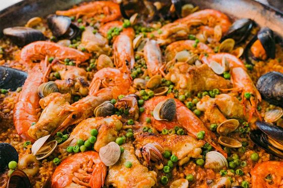 A pan of seafood paella with prawns, mussels, clams, green peas, and rice, garnished with herbs, displayed on a table.