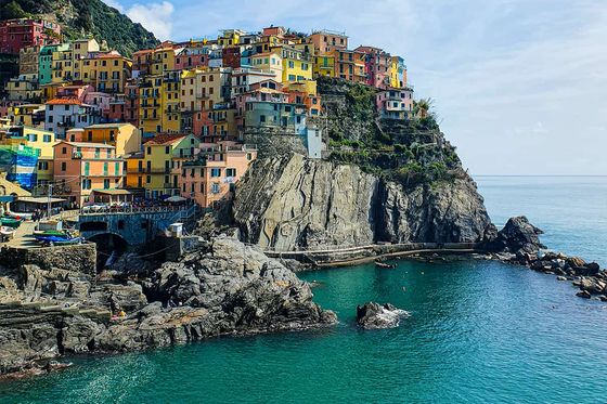Colorful cliffside village overlooking a calm blue sea with rugged rocky shores on a clear day.