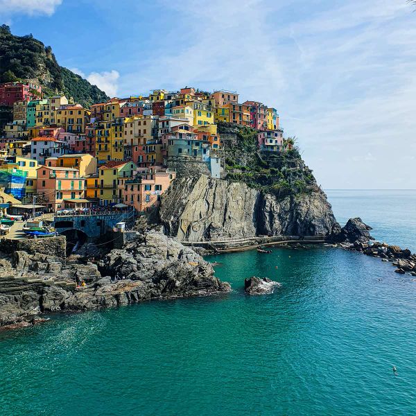 Colorful cliffside village overlooking a calm blue sea with rugged rocky shores on a clear day.
