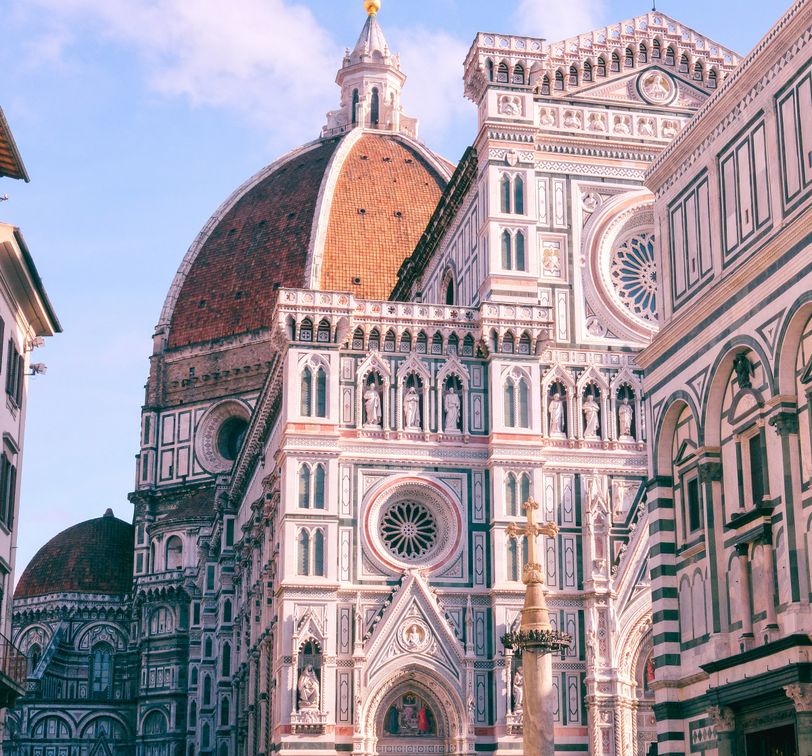 View of Florence Cathedral, featuring its intricate facade, large dome, and decorative marble patterns, set against a clear blue sky.