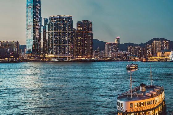 Ferry sailing in a harbor at twilight, with a city skyline and a tall skyscraper in the background.