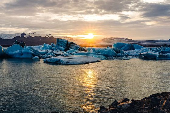 Beautiful sunset over a serene lagoon with floating icebergs and distant mountains under a cloudy sky.