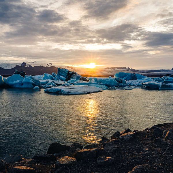 Beautiful sunset over a serene lagoon with floating icebergs and distant mountains under a cloudy sky.