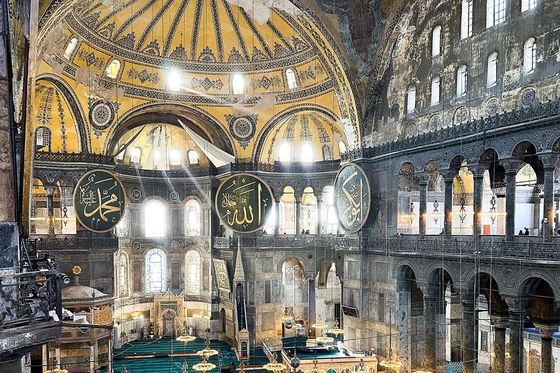 Interior of the Hagia Sophia, featuring grand arches, intricate mosaics, and large circular Arabic calligraphy panels on the walls.