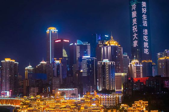 Illuminated cityscape at night with skyscrapers and brightly lit buildings reflecting on a river, featuring vertical Chinese text on a tall tower.