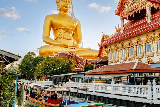A large golden Buddha statue overlooking a boat in the canal.