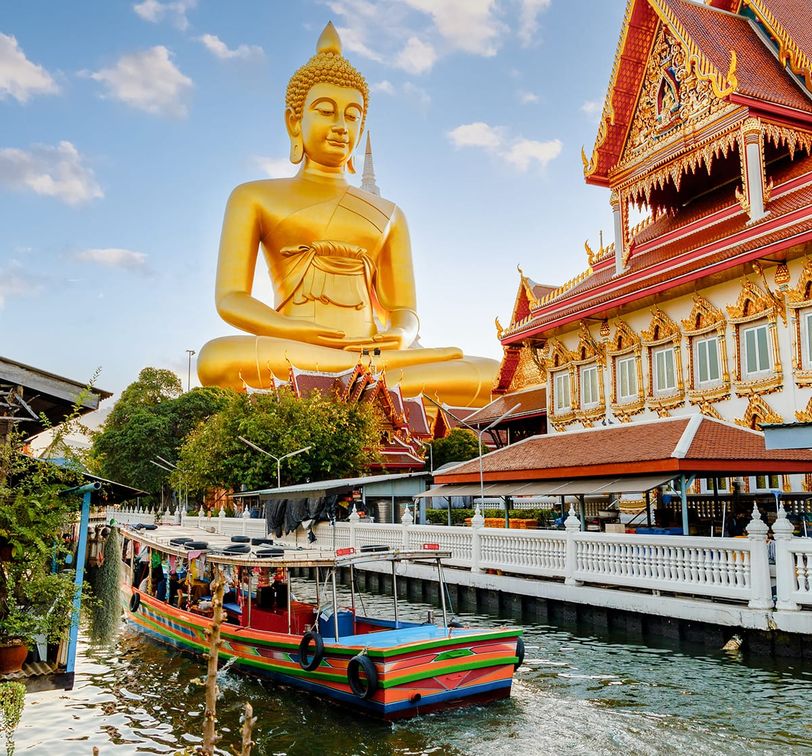 A large golden Buddha statue overlooking a boat in the canal.