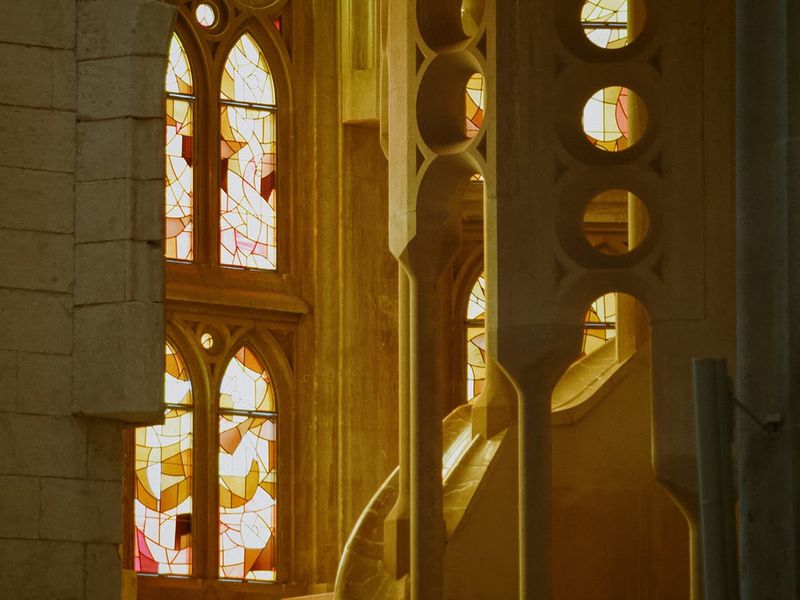 Gothic-style stained glass windows with warm light illuminating a spiral staircase in a cathedral setting.