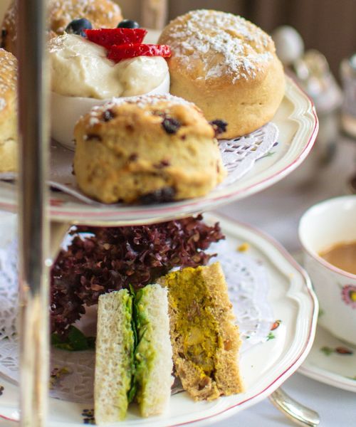Afternoon tea with scones, clotted cream, strawberries, and assorted sandwiches on a tiered stand, accompanied by a cup of tea.
