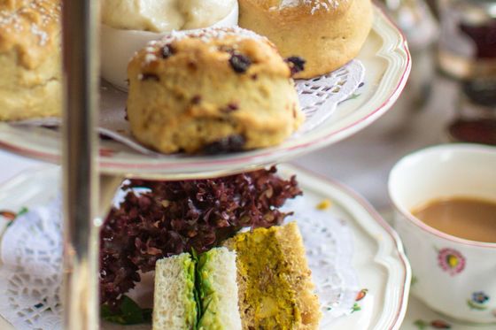 Afternoon tea with scones, clotted cream, strawberries, and assorted sandwiches on a tiered stand, accompanied by a cup of tea.
