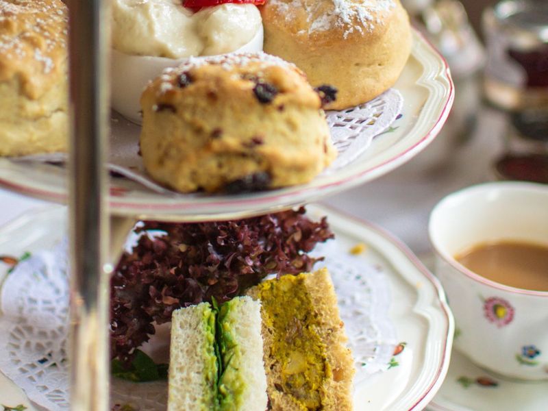 Afternoon tea with scones, clotted cream, strawberries, and assorted sandwiches on a tiered stand, accompanied by a cup of tea.