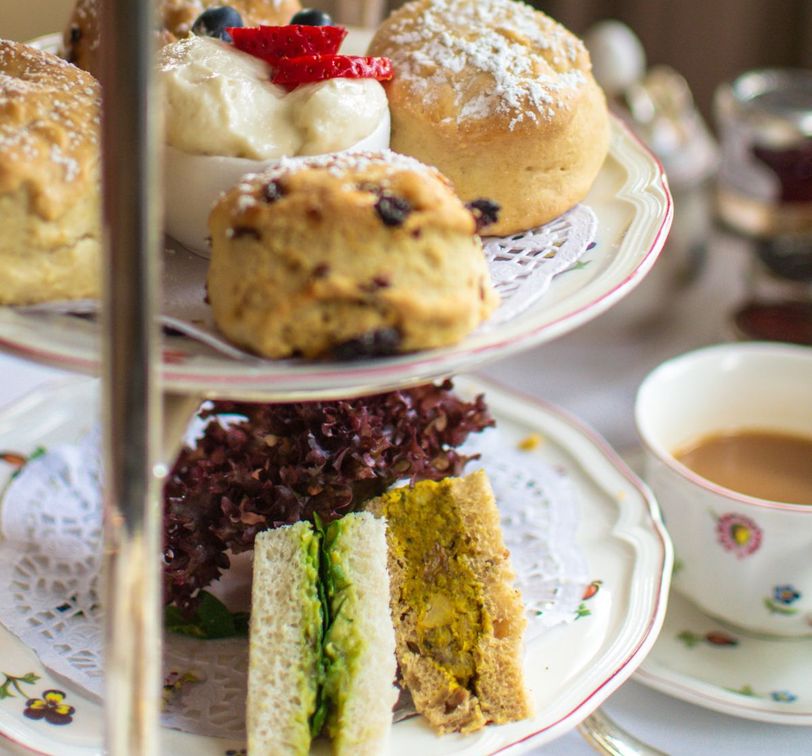 Afternoon tea with scones, clotted cream, strawberries, and assorted sandwiches on a tiered stand, accompanied by a cup of tea.