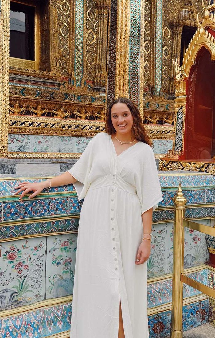 A woman in a white dress standing in front of a colorful gold temple.
