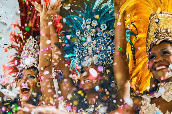 Dancers in vibrant feathered costumes celebrate joyfully amidst colorful confetti.