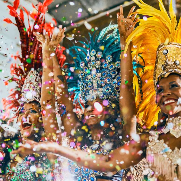 Dancers in vibrant feathered costumes celebrate joyfully amidst colorful confetti.