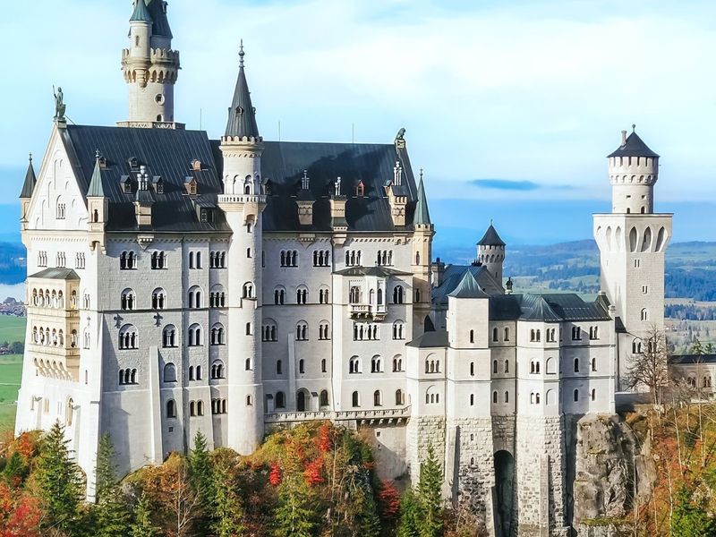 A majestic castle with multiple towers and turrets set against a backdrop of green hills and a blue sky.