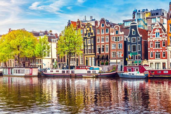 Scenic view of colorful historic buildings and houseboats along a canal in Amsterdam under a blue sky.