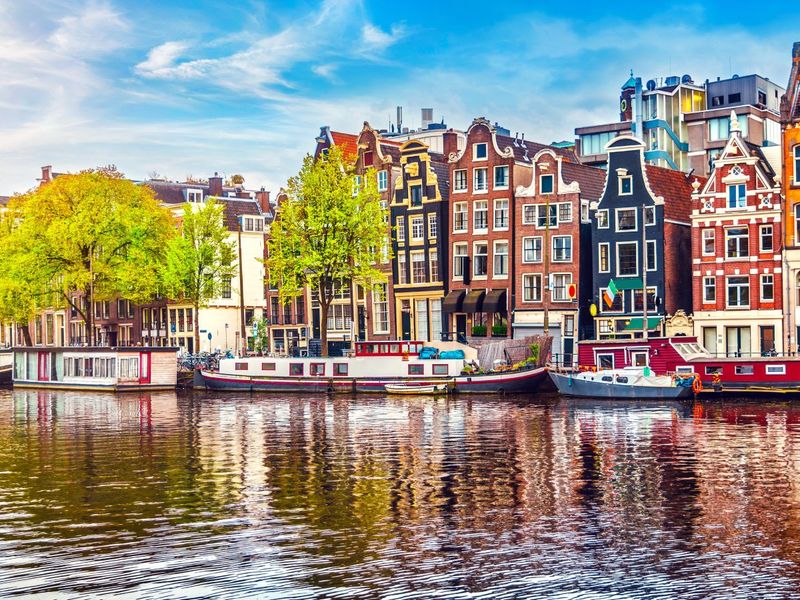 Scenic view of colorful historic buildings and houseboats along a canal in Amsterdam under a blue sky.