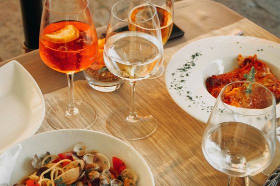A wooden table with plates of seafood pasta and lasagna, accompanied by glasses of orange and clear drinks, elegantly arranged for a meal.