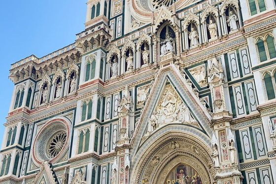 Intricate details of a cathedral facade, featuring ornate sculptures, circular stained glass windows, and architectural embellishments under a clear blue sky.