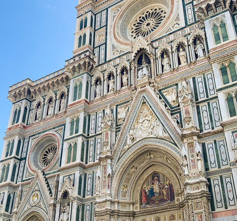 Intricate details of a cathedral facade, featuring ornate sculptures, circular stained glass windows, and architectural embellishments under a clear blue sky.