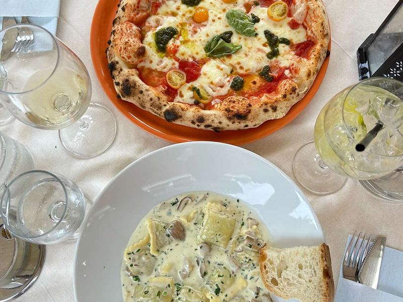 A table with a pizza topped with tomatoes and basil, a pasta dish with creamy sauce and mushrooms, wine glasses, and a slice of bread.