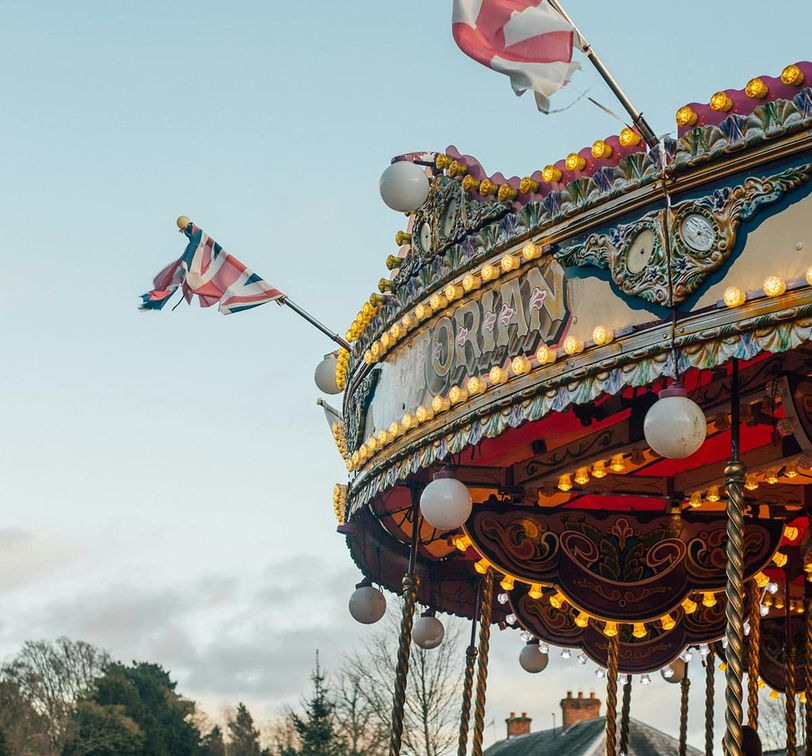 Colorful vintage carousel top with flags and lights against a clear sky and tree-lined background.