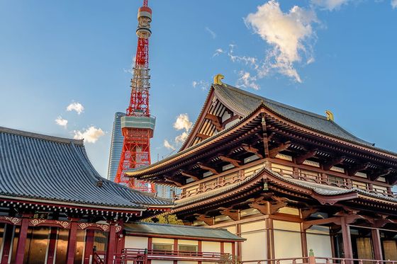 Traditional Japanese temple with ornate wooden architecture in the foreground, Tokyo Tower in the background under a clear blue sky.