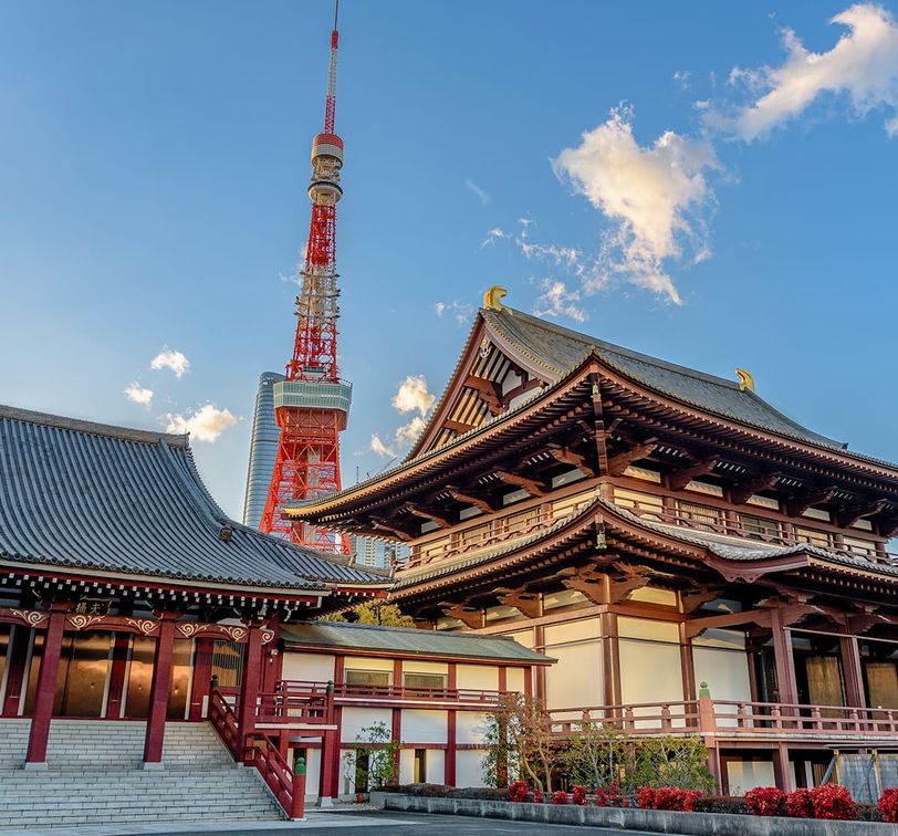 Traditional Japanese temple with ornate wooden architecture in the foreground, Tokyo Tower in the background under a clear blue sky.