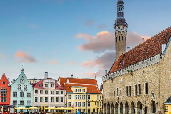 A picturesque town square with colorful historic buildings, a tall spire, and a cobblestone ground beneath a vibrant sky.