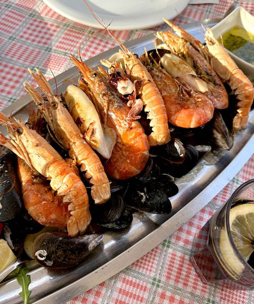 A platter of seafood with prawns, mussels, and clams on a checkered tablecloth, accompanied by lemon wedges and dipping sauce.