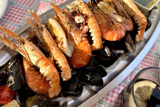 A platter of seafood with prawns, mussels, and clams on a checkered tablecloth, accompanied by lemon wedges and dipping sauce.