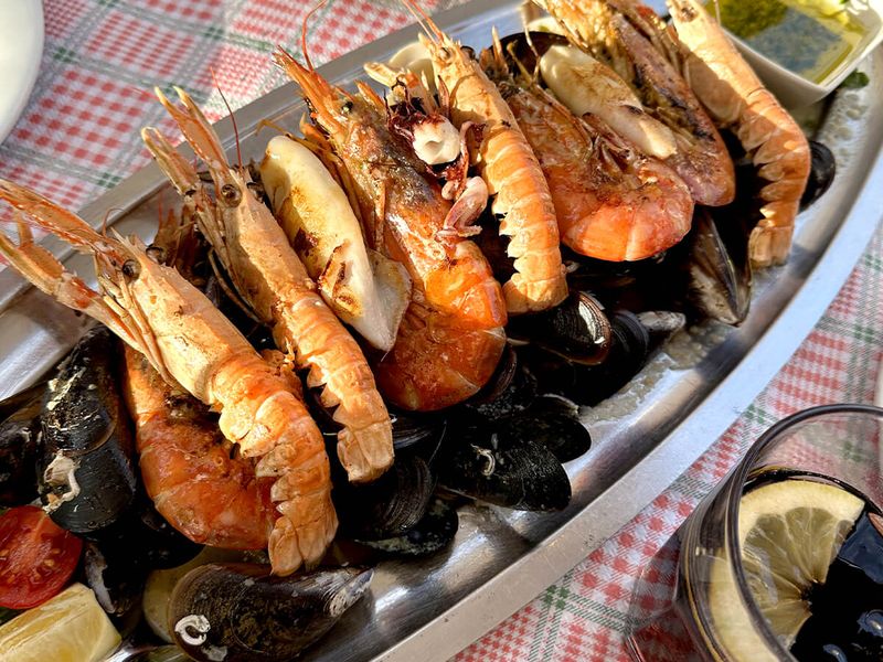 A platter of seafood with prawns, mussels, and clams on a checkered tablecloth, accompanied by lemon wedges and dipping sauce.