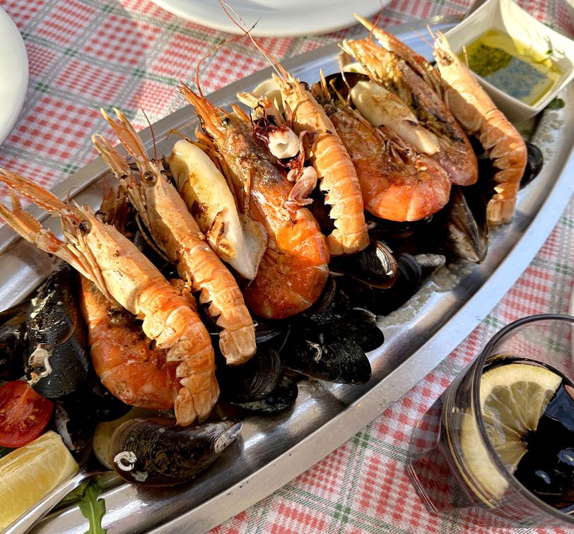 A platter of seafood with prawns, mussels, and clams on a checkered tablecloth, accompanied by lemon wedges and dipping sauce.