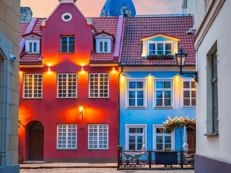 Colorful historic buildings with red and blue facades on a cobblestone street at dusk, featuring warm lighting and a visible church dome.