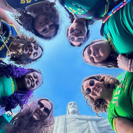A group of people in a circle, smiling and looking down at the camera, with the Christ the Redeemer statue visible in the background.