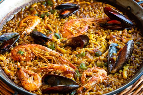 Paella dish with prawns, mussels, and vegetables in a large pan, showcasing vibrant colors and textures.