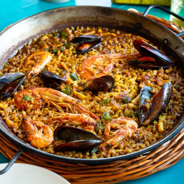 Paella dish with prawns, mussels, and vegetables in a large pan, showcasing vibrant colors and textures.