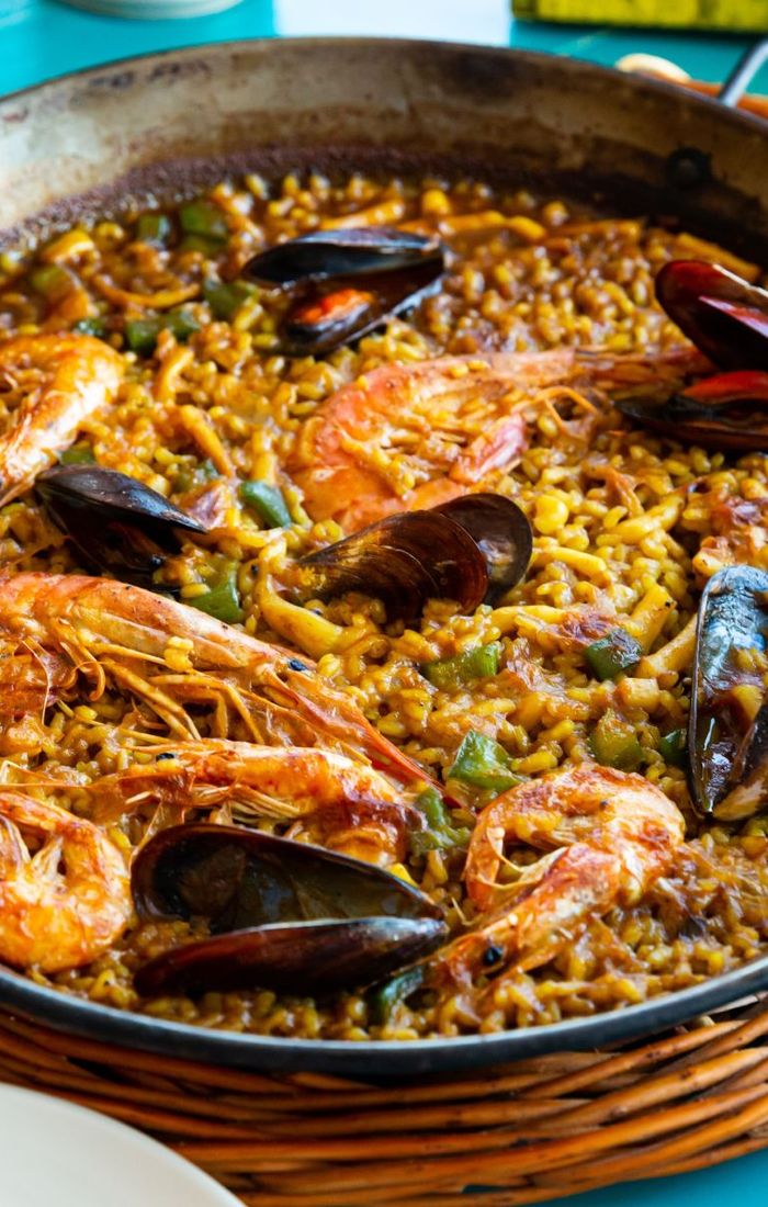 Paella dish with prawns, mussels, and vegetables in a large pan, showcasing vibrant colors and textures.