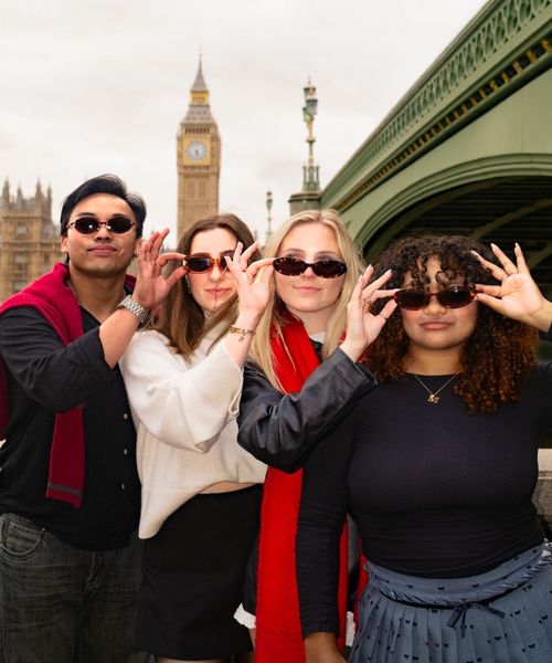 Four people pose playfully with sunglasses in front of Big Ben, standing near the Westminster Bridge in London.