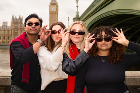 Four people pose playfully with sunglasses in front of Big Ben, standing near the Westminster Bridge in London.
