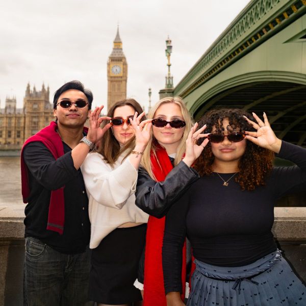 Four people pose playfully with sunglasses in front of Big Ben, standing near the Westminster Bridge in London.