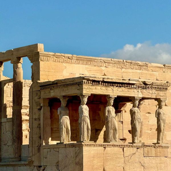 The Erechtheion's Caryatids on the Acropolis, Athens, with six stone maidens supporting the portico under a clear blue sky.