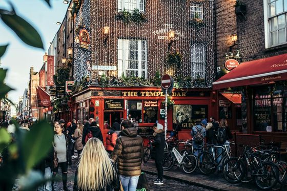 People walking outside The Temple Bar in Dublin, Ireland, with festive lights and bicycles nearby on a cobblestone street.