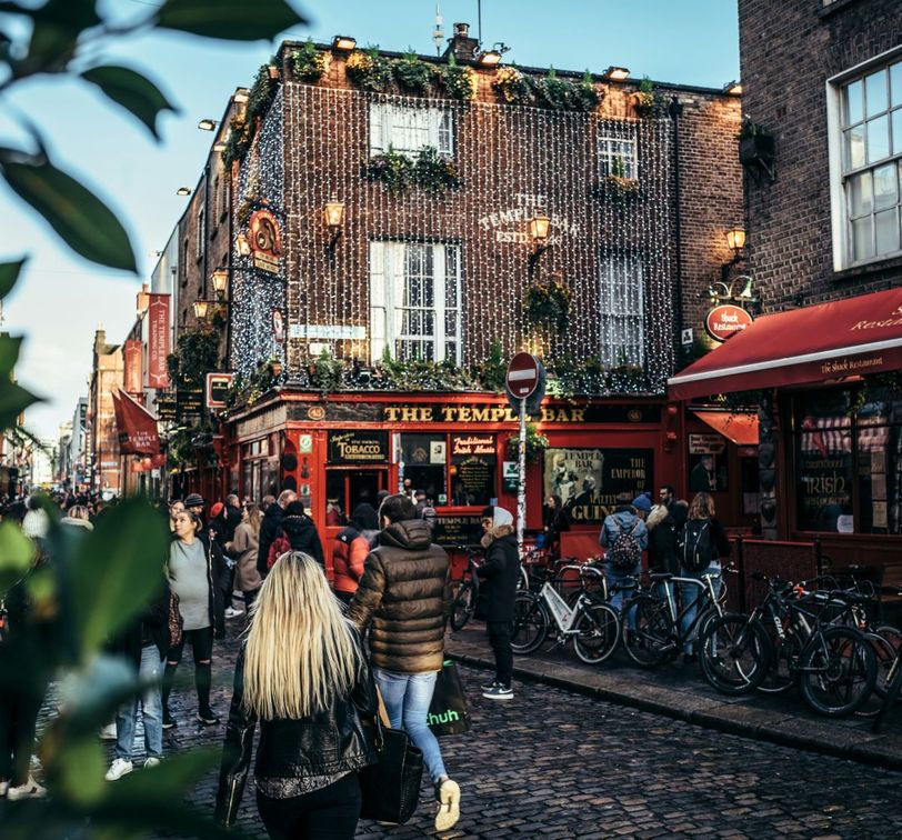 People walking outside The Temple Bar in Dublin, Ireland, with festive lights and bicycles nearby on a cobblestone street.