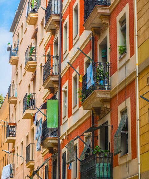 Colorful apartment buildings with balconies adorned with plants and laundry, set against a blue sky.