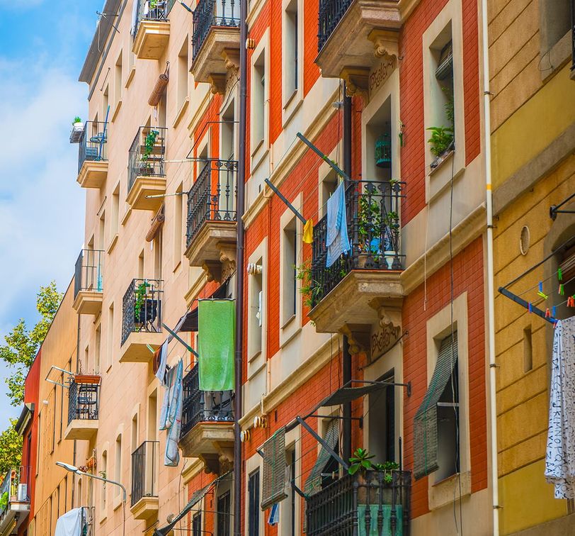 Colorful European apartment buildings with balconies, laundry hanging, and potted plants. Bright sky in the background.